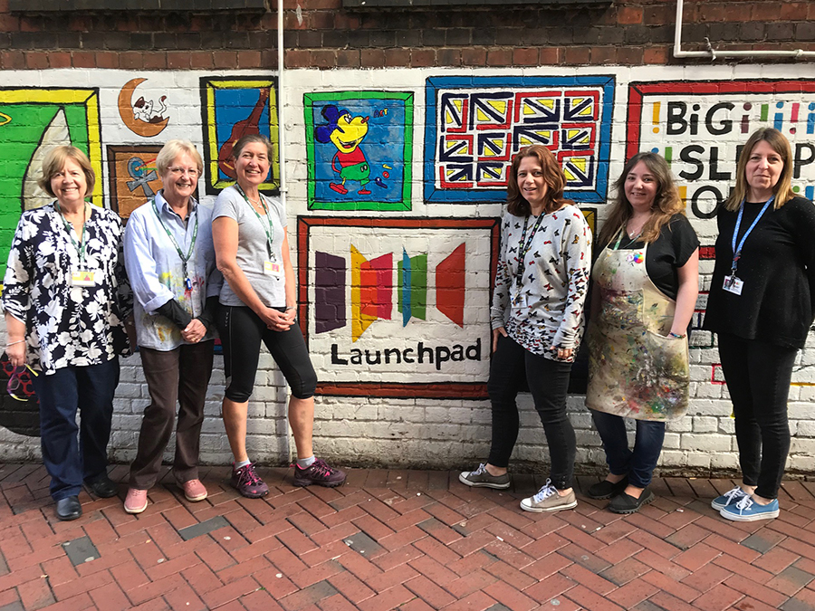 volunteer women standing in front of wall with launchpad logo on it