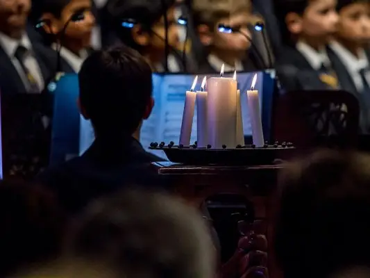 Man playing piano with choir in background and candles in foreground at Carols by Candlelight
