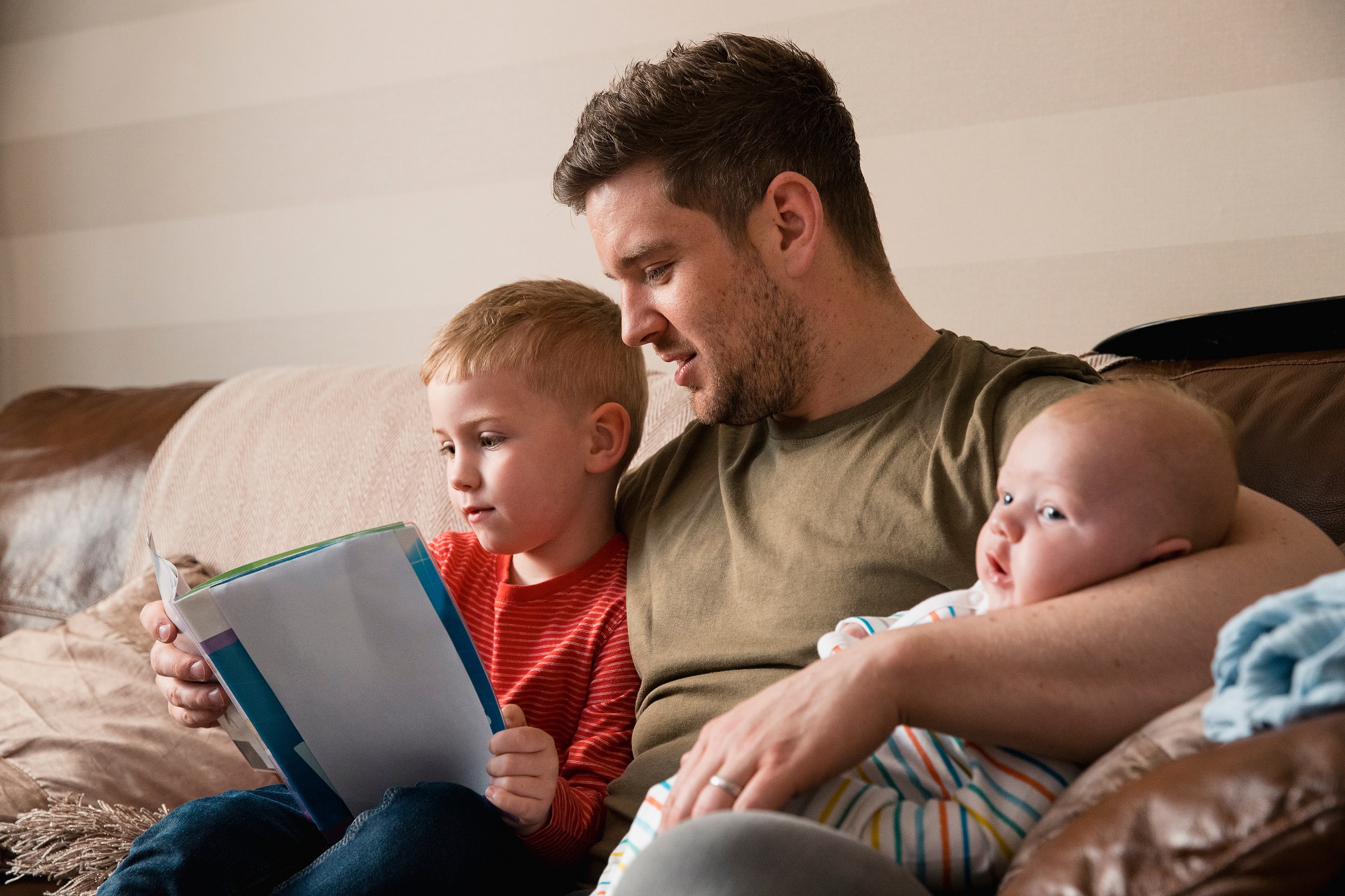 Stock image on man holding two young children sat on sofa