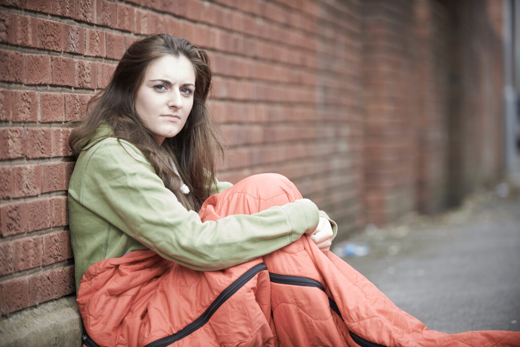 A stock image of a young homeless female in sleeping bag.
