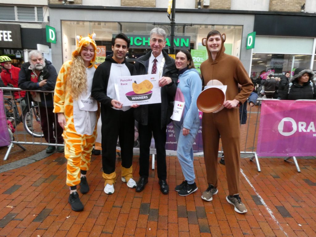 Photo of the winners of the 2024 Pancake Race - people in fancy dress racing as they flip pancakes.