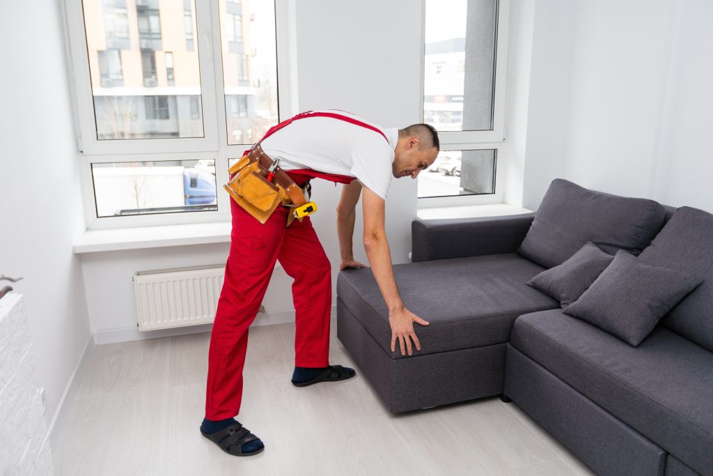 A removal man moving a grey sofa in a living room