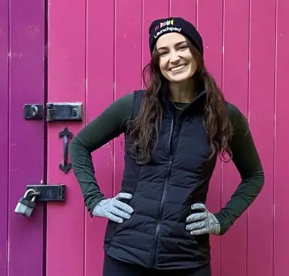 Julia - who will be running the London Marathon for Launchpad, standing in front of a pink door wearing a launchpad hat and her running gear