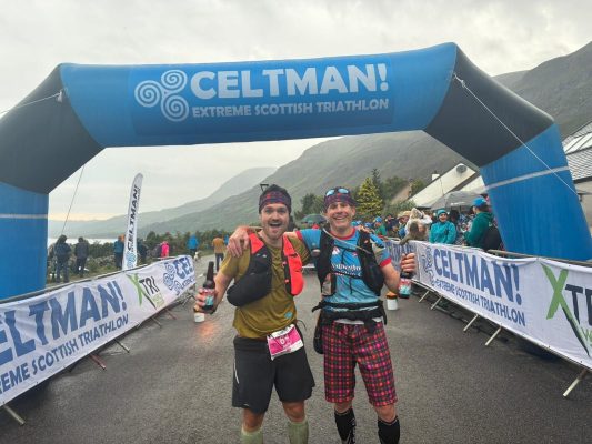 Two men standing by the finish line after the ironman challenge in Scotland.