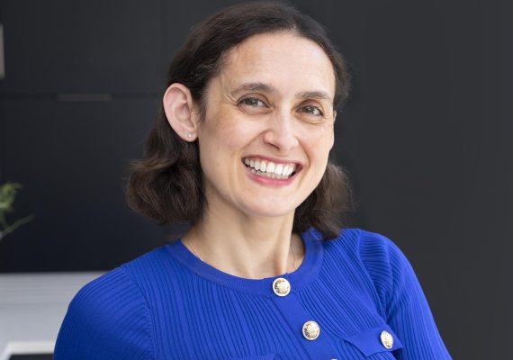 Woman with dark hair and blue jacket smiling