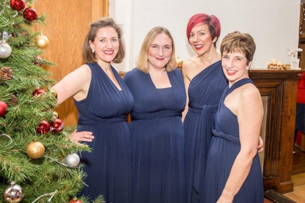 Four ladies wearing a blue dress standing by a Christmas tree
