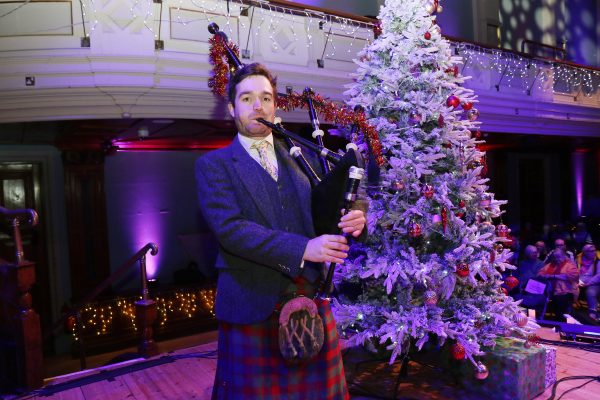 Man in kilt playing the bagpipes standing by a Christmas tree