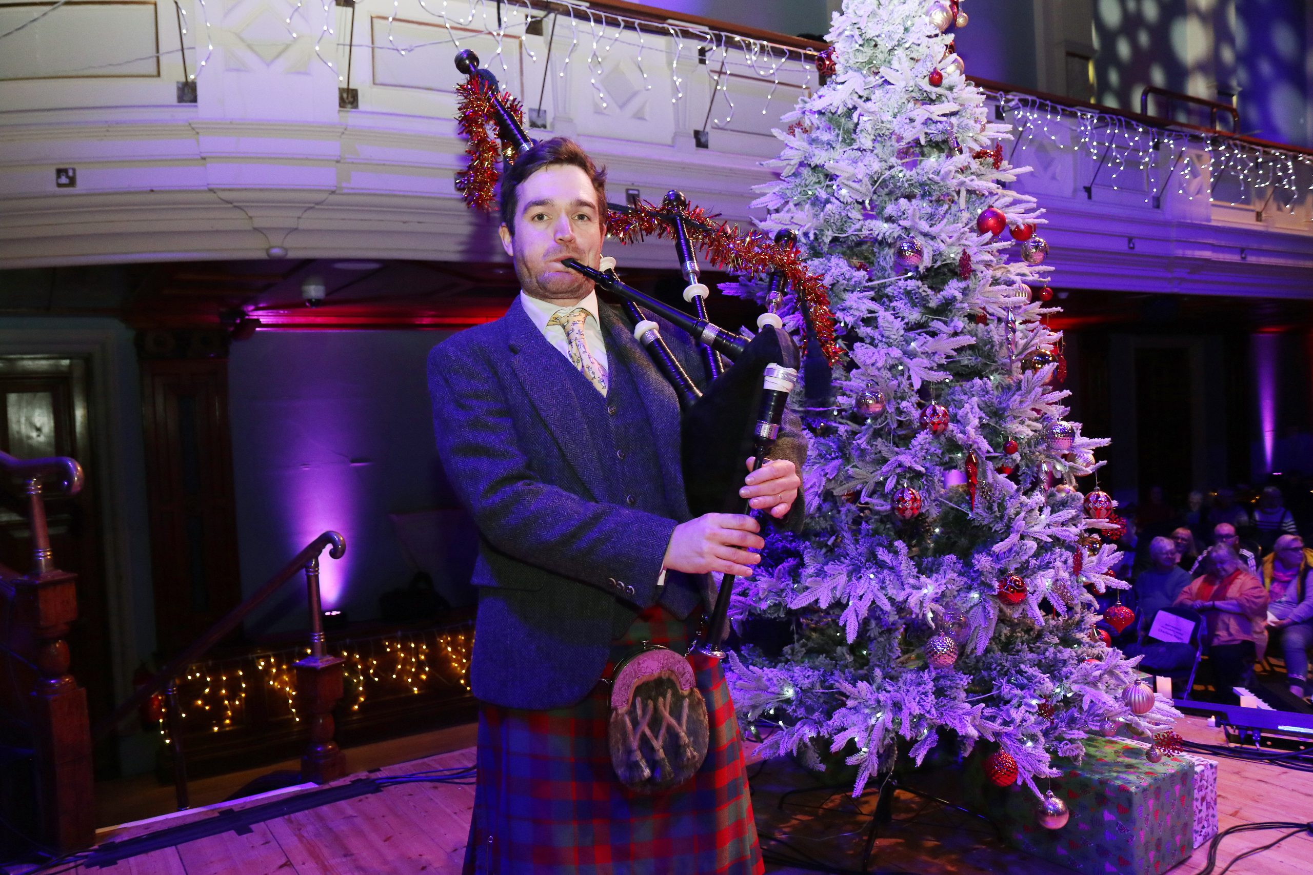 Man in kilt playing the bagpipes standing by a Christmas tree