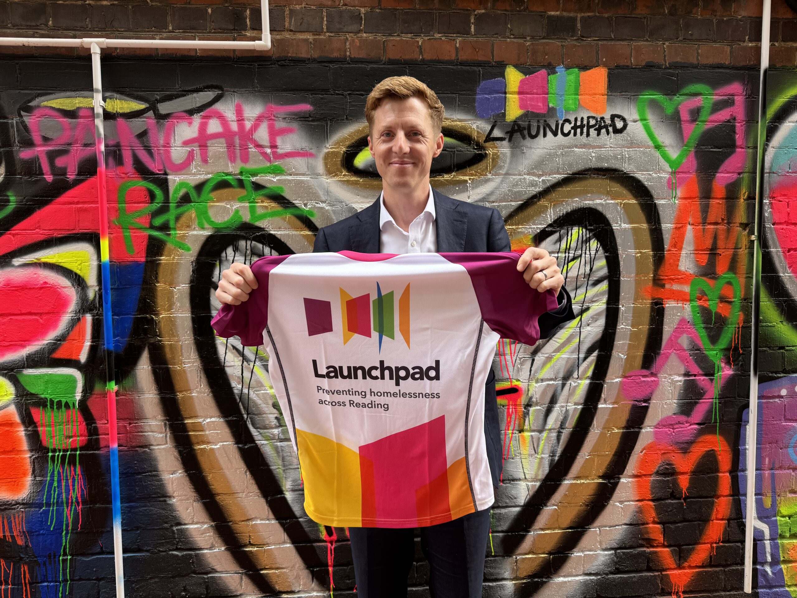 man with Launchpad running shirt standing in front of mural