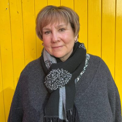 Head and shoulders photo of volunteer Kate standing in front of yellow door