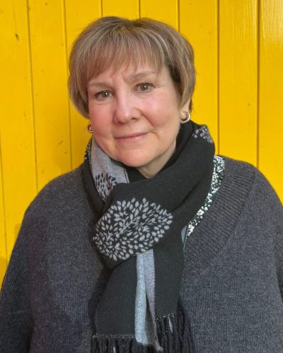 Head and shoulders photo of volunteer Kate standing in front of yellow door